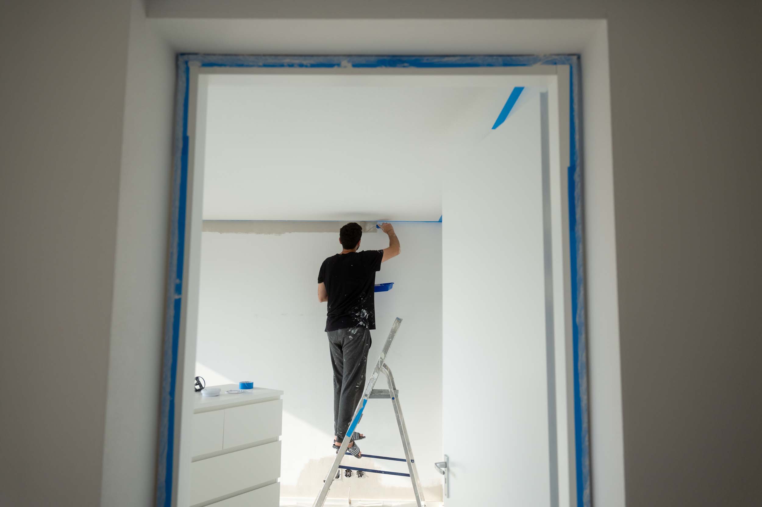 Painter painting a white wall using a ladder